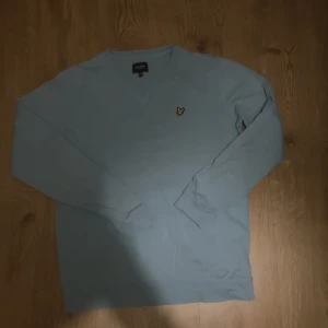 Ljusblå långärmad tröja Lyle & Scott - Snygg ljusblå långärmad tröja från Lyle & Scott med deras klassiska gul fågel-logga på bröstet. Tröjan har rund hals och är gjord i mjuk bomull, perfekt för chill dagar. Enkel och stilren design som funkar till jeans eller shorts.