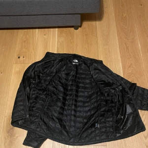 Svart pufferjacka från The North Face - Säljer en svart pufferjacka från The North Face i storlek L. Jackan har quiltad design, dragkedja och är tillverkad i syntetmaterial. Perfekt för kalla dagar och har en clean look med logga på bröstet och ärmen.