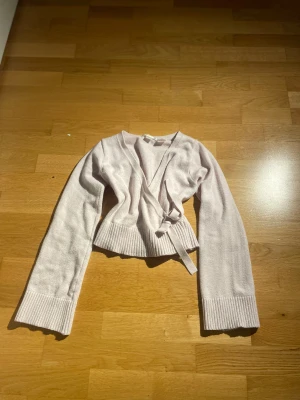 Ljusrosa omlott kofta med knyt - Superfin ljusrosa omlott kofta från Gina tricot med knyt i midjan och breda ribbade muddar. Croppad modell med långärmade ärmar och mjukt stickat material som är perfekt för lager-på-lager. Snygg att matcha med jeans eller kjol.