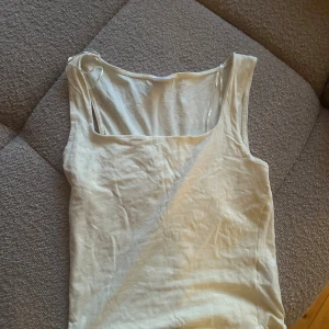 Vit linnetopp med fyrkantig ringning - Snygg vit linnetopp med breda axelband och fyrkantig ringning. Perfekt att styla med jeans eller kjol för en clean look. Tillverkad i mjuk bomull som känns skön mot huden. Enkel och stilren design som funkar till många outfits.