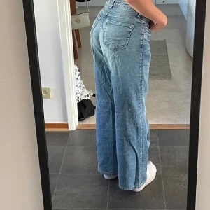 Blåa wide jeans med hög midja - Säljer ett par ljusblå jeans med medel hög midja och raka, vida ben. Klassisk femficksmodell med knapp- och dragkedjestängning. Perfekta för en avslappnad och trendig look.