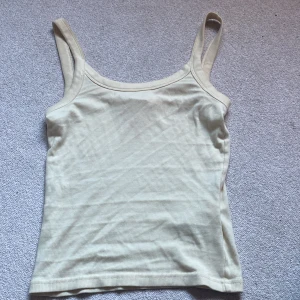 Beige ribbad linnetopp - Säljer en enkel och stilren gula linnetopp med smala axelband och ribbad struktur. Toppen har en rundad halsringning och är figurnära i modellen. Perfekt att styla med jeans till en chill look. Lite uttöjd passar för S och uppåt men beror på hur du vill att den ska sitta!