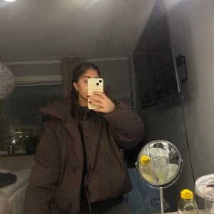 Brun pufferjacka med stor krage - Säljer en brun pufferjacka med riktigt stor och cool krage. Jackan har en loose passform och är perfekt för kalla dagar. Den är tillverkad i ett syntetmaterial och har knappar framtill. Passar dig som gillar oversized och vill ha en jacka som sticker ut. Har prislapp kvar och köptes för 860