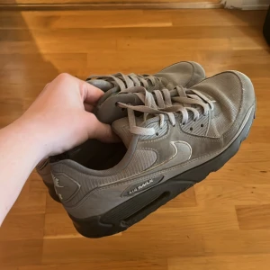 Grå Nike Air Max sneakers - Säljer ett par grå Nike Air Max sneakers med klassisk design och synlig Air-sula. Skorna har snörning, rund tå och platt sula. Ovandelen är i syntet och mesh för bra ventilation. Snyggt Nike-märke på sidan och bak. Perfekt för dig som gillar streetwear pris går att diskutera