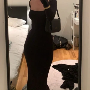 Svart långärmad långklänning - Säljer en svart långklänning med långärmad design och figurnära passform. Klänningen har en snygg, fyrkantig urringning och är tillverkad i ett stretchigt material som framhäver siluetten. Perfekt för dig som gillar stilrena och eleganta looks.
