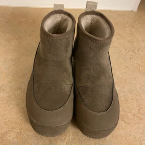 Tretorn Alunda hybrid strl 36 - Säljer ett par beige boots från Tretorn med mjukt vitt foder på insidan. Skorna har en rund tå, platt sula med grovt mönster och breda dragflikar bak med Tretorn-logga. Utsidan är i mocka och syntet, perfekta för kalla dagar. Köpta sent förra säsongen så mkt lite använda.