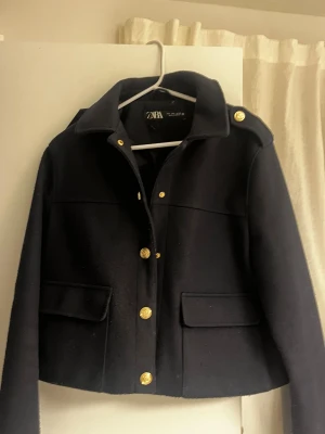 Svart jacka från Zara med guldknappar - Snygg svart skepparkavaj från Zara med guldknappar och axelklaffar. Jackan har två stora fickor framtill. Kommer inte till användning längre. Storleken är L men sitter inte som om det vore det, ser och känns mindre.