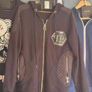 ”AIR” hoodie från Philipp Plein  - Svart hoodie från Philipp Plein med stort metalliskt PP-emblem på bröstet, quiltade detaljer vid axlar och fickor samt dragkedja framtill. Hoodien har huva med snörning och ribbade muddar. Modellen ”AIR” som var en otrolig limited edition utgåva. Samma modell rappare Yasin hade i sin ”chicago” musik video. Pris går att diskutera 