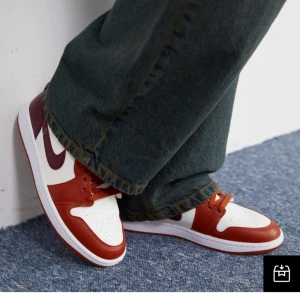 Nike Jordan 1 röd och vit sneakers - Säljer ett par Nike Jordan 1 sneakers i rött och vitt med mörkröda detaljer. Skorna har klassisk snörning, rund tå och platt sula. Ikonisk design med perforerad tåbox och kontrasterande Swoosh på sidan. Perfekta för dig som gillar streetwear och vill sticka ut.