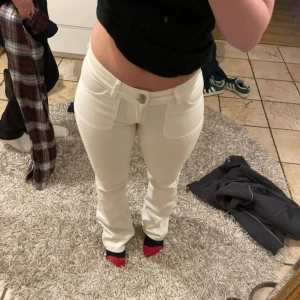 Vita bootcut jeans med fickdetaljer - Snygga vita jeans med bootcut passform och låg midja. Framtill finns två stora fickor och baktill fickor med lock och knapp. Jeansen har dragkedja och knapp i midjan, tillverkade i mjuk bomull. Perfekta för dig som gillar stilrena och fräscha byxor. Finns två små fläckar som ej syns(se bilder)