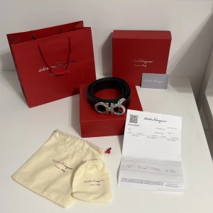 Svart skärp från Salvatore Ferragamo - Exklusivt svart bälte från Salvatore Ferragamo med en ikonisk, rundad silverfärgad spänne med logotyp. Bältet är tillverkat i slätt skinn och levereras med originalförpackning, dustbags och kvitto. Perfekt accessoar för att lyfta din outfit med lyxig känsla.