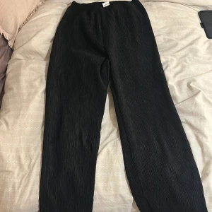 Svarta plisserade byxor från shein storlek S - Svarta byxor med plisserad struktur och avslappnad passform. De har elastisk midja och raka ben, vilket ger en skön och trendig look. Perfekta för dig som gillar bekväma och stilrena plagg med lite extra edge.
