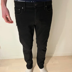 Svarta tapered jeans från Jack & Jones - Snygga svarta jeans från Jack & Jones med tapered passform. Klassisk femficksdesign, knapp och dragkedja i midjan. Jeansen är tillverkade i mjukt bomullsmaterial med lite stretch för extra komfort. Perfekt för dig som gillar stilrena och moderna byxor.