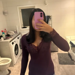 Vinröd tröja med spetsdetaljer - Säljer en vinröd tröja  med lång ärm och snygga spetsdetaljer vid v-ringad hals och ärmslut. Tröjan har en slim passform och är perfekt för dig som gillar stilrena och feminina plagg. Materialet känns mjukt och följsamt mot kroppen.