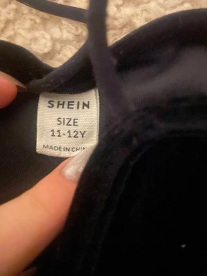 Svart sammetsklänning från Shein - Supersnygg svart kortklänning från Shein i mjuk sammet. Klänningen har smala axelband och en figurnära passform som ger en stilren och modern look. Perfekt för dig som gillar minimalistisk stil och vill sticka ut med en klassisk vibe.