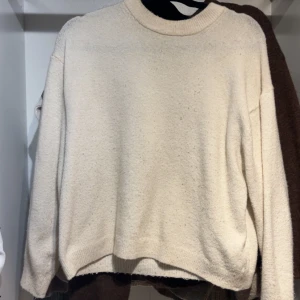 vit stickad tröja med rund hals - Mysig vit stickad tröja med rund hals och långa ärmar. Tröjan har en enkel och clean design med ribbade muddar vid hals, ärmslut och nederkant. Perfekt för att hålla sig varm under kyliga dagar.