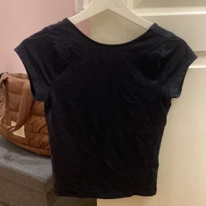 Mörk blå croppad topp med öppen rygg - En mörk blå croppad topp i bomull med korta ärmar och en djup, öppen rygg. Enkel och stilren design som passar perfekt till jeans eller kjol. Mjuk och skön mot huden, perfekt för dig som gillar minimalistiska plagg.