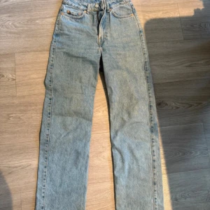 ljusblå jeans straight fit - Säljer ett par klassiska Weekday Rowe jeans i ljusblå tvätt med raka ben och hög midja. Jeansen har fem fickor, knappgylf och  läderpatch bak i midjan. Perfekt för dig som gillar retrostil och tidlös denim.