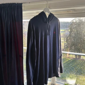 Mörkblå hoodie från Polo Ralph Lauren XL - Snygg mörkblå hoodie från Polo Ralph Lauren i storlek XL. Tröjan har huva med snörning och en röd broderad logga på bröstet. Tillverkad i mjuk bomull och har långa ärmar. Perfekt för chill dagar och enkel att matcha med jeans eller joggers.