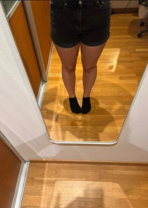 Svarta högmidjande jeansshorts från H&M - Säljer ett par svarta jeansshorts från H&M med  hög midja i storlek 36. Klassisk femficksmodell med knapp och dragkedja framtill. Snygg, tight passform och tillverkade i mjuk bomullsdenim. Perfekta för dig som gillar en clean och enkel look.