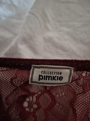 Vinröd ribbad topp med spets från Pimkie - Säljer en vinröd långärmad topp från Pimkie med ribbad struktur och snygg spetsdetalj vid v-ringningen. Toppen har en slim passform och är tillverkad i mjukt syntetmaterial. Perfekt för dig som gillar detaljer och vill ha en stilren look.