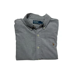 Ralph Lauren Skjorta - Klassisk grå skjorta från Polo Ralph Lauren med button-down krage och broderad logga på bröstet. Skjortan har knappar framtill och är perfekt för en stilren look. Tillverkad i mjuk bomull för maximal komfort. Hör av dig vid minsta fundering!