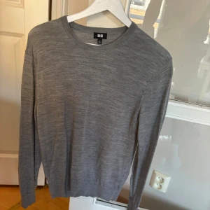 Grå merinoulltröja från Uniqlo - Snygg grå tröja från Uniqlo i mjuk merinoull. Klassisk rund hals och långärmad modell med diskret ribbade muddar vid ärmslut och nederkant. Perfekt för dig som gillar stilrena och enkla plagg med skön passform.