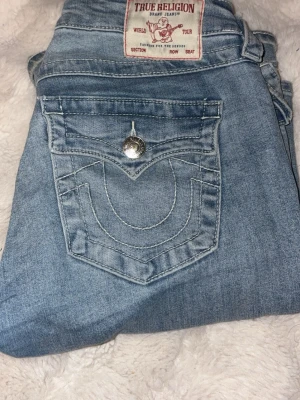 Lågmidjade, ljusblå True religion jeans i modell joey - Super fina jeans i storlek 26 vilket motsvarar S/M. De är bara använda några fåtal gånger och är som nya. De är väldigt Lågmidjade!💗💗