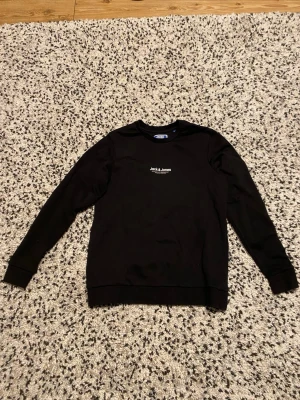 Svart sweatshirt från Jack & Jones - En stilren svart sweatshirt från Jack & Jones med diskret logga på bröstet. Tröjan har rund halsringning, långa ärmar och är perfekt för dig som gillar enkel och clean stil.