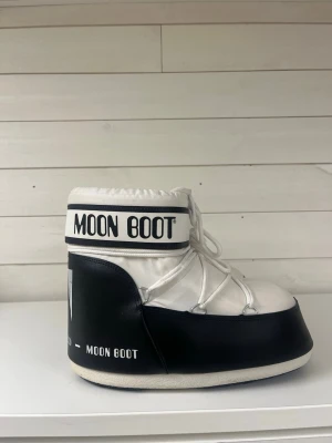 Svarta och vita Moon Boots - Moon Boot i svart och vitt med tydlig logga runt skaftet. Skorna har snörning framtill och en vadderad, chunky siluett. Yttermaterialet är syntet och de har en platt sula. Perfekta för vinter och snöiga dagar. 