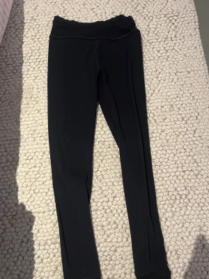 Svarta leggings från SOC, stl 134/140 - Svarta leggings från SOC med stretchigt material och snygg vågig kant upptill. Perfekta för träning eller chill, sitter tajt och har en mjuk känsla. Materialet är syntet och håller dig torr och bekväm. Klassisk och enkel design som funkar till det mesta.