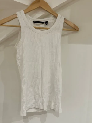 Vit ribbad linnetopp från Vero Moda - Säljer en enkel och stilren vit ribbad linnetopp från Vero Moda i storlek XS. Toppen är ärmlös med rund halsringning och har en tight passform. Perfekt att matcha med jeans eller kjol för en clean look.