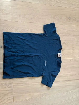 Mörkblå t-shirt från MC2 Saint Barth - Säljer en mörkblå t-shirt från MC2 Saint Barth med diskret broderad logga på bröstet. Klassisk rund hals och korta ärmar. Tillverkad i mjuk bomull som känns skön mot huden. Perfekt för en avslappnad och stilren look.