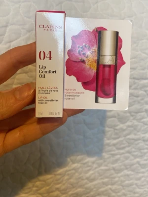 Clarins Lip Comfort Oil 04 Pitaya - Clarins Lip Comfort Oil i färgen 04 Pitaya är ett läppolja med en härlig rosa ton. Kommer i en genomskinlig tub med guldfärgat lock och applikator. Innehåller sötbriarrosolja som ger näring och glans till läpparna. Förpackningen är smidig och lätt att ta med. Oöppnad, oanvänd