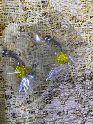 Glittriga navelpiercingar i olika färger - Säljer flera navelpiercingar med glittrande kulor i färgerna gul, röd, lila, blå och svart. Staven är i metall och kulorna är täckta av små gnistrande stenar. Perfekt för dig som vill ha något färgglatt och snyggt till din piercing.