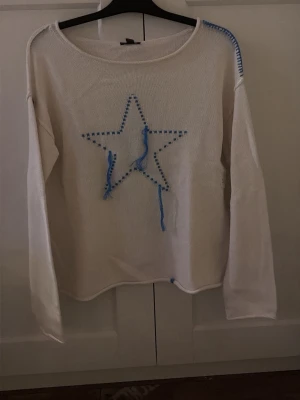 Vit stickad tröja med blå stjärna - Vit stickad tröja med lång ärm och en stor blå stjärna broderad framtill. Aldrig använd 💞
