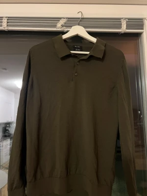 Mörkbrun merinoull pikétröja Massimo Dutti - Säljer en stilren mörkbrun långärmad pikétröja från Massimo Dutti i mjuk merinoull. Tröjan har klassisk krage, knappar framtill och en clean look som passar perfekt till både jeans och chinos.