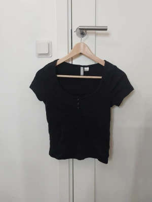 Svart kortärmad topp från H&M Divided - En svart, enkel topp från H&M Divided med rund halsringning och tre små knappar framtill. Modellen är kortärmad och har en något croppad passform❣️