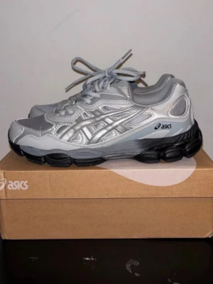 ASICS skor - Säljer ett par riktigt snygga ASICS sneakers i silver med detaljer i mesh och syntet. Skorna har en chunky svart sula och klassisk snörning. Perfekta för dig som gillar sportig stil och vill ha något som sticker ut. Levereras i originalkartong.