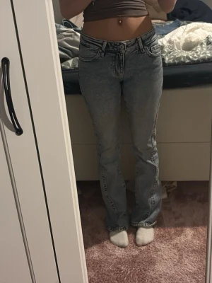 Grå bootcut jeans med broderade fickor - Säljer ett par gråa bootcut jeans med snyggt broderade bakfickor och klassisk femficksdesign. Jeansen har låg midja och är i ett tvättat denimtyg som ger en cool vintagekänsla. Perfekta för dig som gillar en avslappnad men trendig stil.