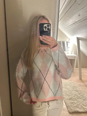 Pastellrutig stickad tröja - Supermysig stickad tröja i pastellrosa och vitt med rutigt argylemönster. Tröjan har rund hals, ribbade muddar och en loose fit. Perfekt för dig som gillar en söt och chill stil.