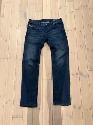 Mörkblå raka jeans från Diesel - Säljer ett par mörkblå jeans från Diesel med klassisk femficksdesign och raka ben. Jeansen har snygga slitningar framtill och en tydlig Diesel-patch bak i midjan. Materialet är stretchigt denim i bomull och passformen är regular/straight! Inte mycket använda!