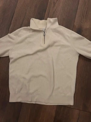 Beige ribbad half zip tröja H&M - Säljer en beige ribbad tröja från H&M med halv dragkedja och hög krage. Slim fit-modell med långa ärmar och mjukt material som passar perfekt till lager på lager. Enkel och clean look som funkar till allt.