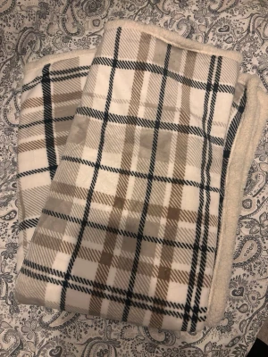 Rutig sherpapläd från HOME - Mysig sherpapläd från HOME i storlek 130x160 cm. Ena sidan är supermjuk och fluffig i vitt, andra sidan har ett rutigt mönster i beige, brunt och svart. Tillverkad i 100% polyester och certifierad enligt OEKO-TEX Standard 100.