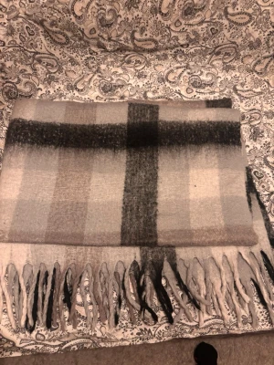 Rutig pläd med fransar - Säljer en mysig pläd i ull med stora rutor i grått, beige och svart. Filten har långa fransar längs nederkanten som ger en chill vibe. 