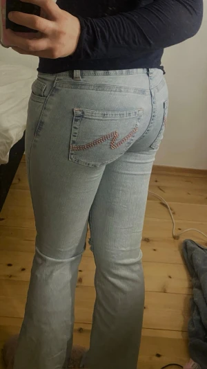 Jeans från Nelly😍💘 - Säljer ett par ljusblå bootcut jeans från Nelly med slitna hål på båda knäna och snygga broderade detaljer på bakfickorna. Jeansen är lågmidjade och stretchiga. Knappt använda. Dom är i short varianten
