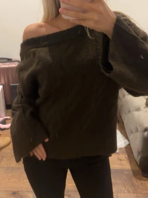 Mörkbrun offshoulder stickad tröja - Säljer en mörkbrun stickad tröja med offshoulder-design och breda ärmar. Tröjan har en loose passform och är perfekt för dig som gillar en avslappnad och trendig stil. Supermjuk och skön att bära under kyliga dagar.