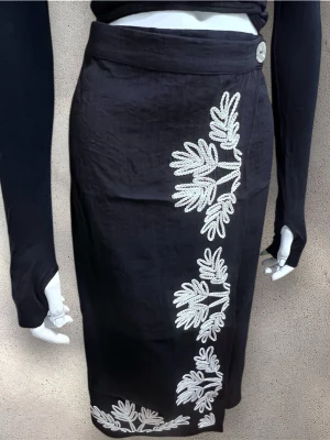 Svart långkjol med broderade detaljer - Snygg svart långkjol med bege broderade bladmönster längs sidan och nederkanten. Kjolen har en rak passform och stängs med en knapp i midjan. Tillverkad i ett mjukt tyg som ger en clean och stilren look. #H&M #hm #Kjol