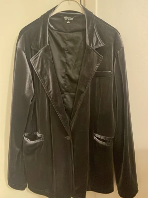 Svart sammetskavaj från Diamonds by Tindra - Säljer en svart sammetskavaj från Diamonds by Tindra i storlek L. Kavajen har klassisk krage, en knapp framtill och fickor med sammetskant. Perfekt för dig som vill ha en elegant och mjuk look.