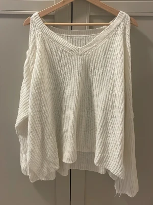 Vit stickad tröja med snörning - Säljer en oversized vit stickad tröja med v-ringning och snygga snörningsdetaljer på ärmarna. Tröjan har lång ärm och ribbade muddar. Perfekt för dig som gillar en chill och trendig look.